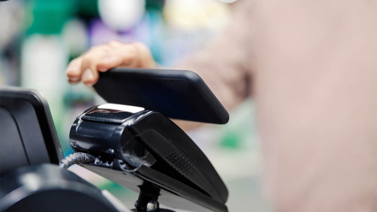 Small business owner using smartphone for contactless payment at a POS terminal, illustrating managed IT services in NYC in action.