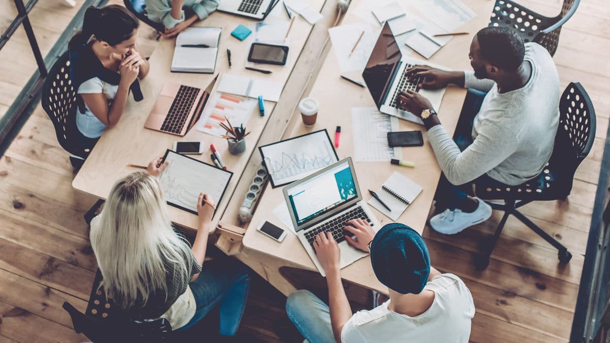 NYC small business team meeting around a table with laptops and charts while planning their cybersecurity strategy.