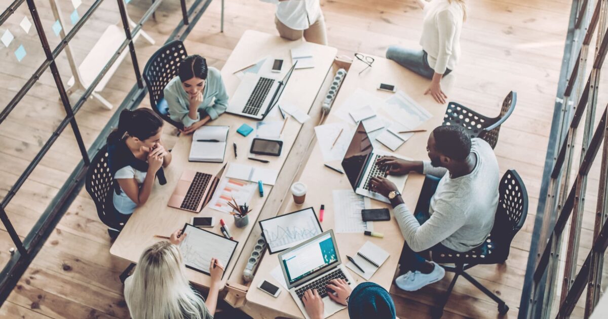 NYC small business team meeting around a table with laptops and charts while planning their cybersecurity strategy.